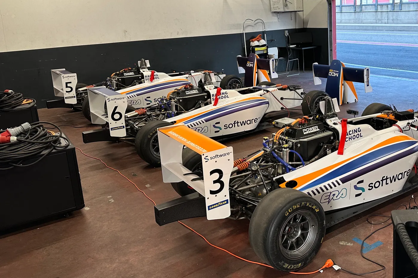 Three ERA formula cars on charge in the garage, HV cables running to each