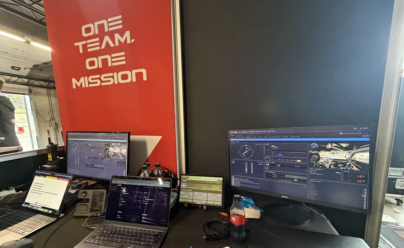 Laptops and a monitor running Apex Insights on a desk in a race garage